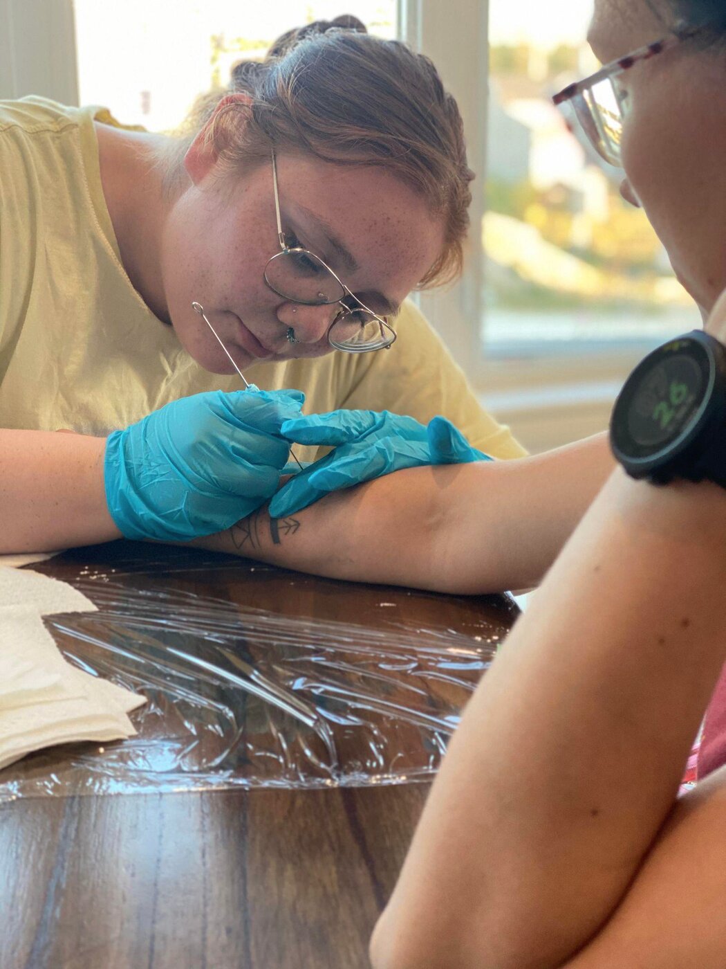 Erica in gloves, hand-poking a tattoo on a client's forearm